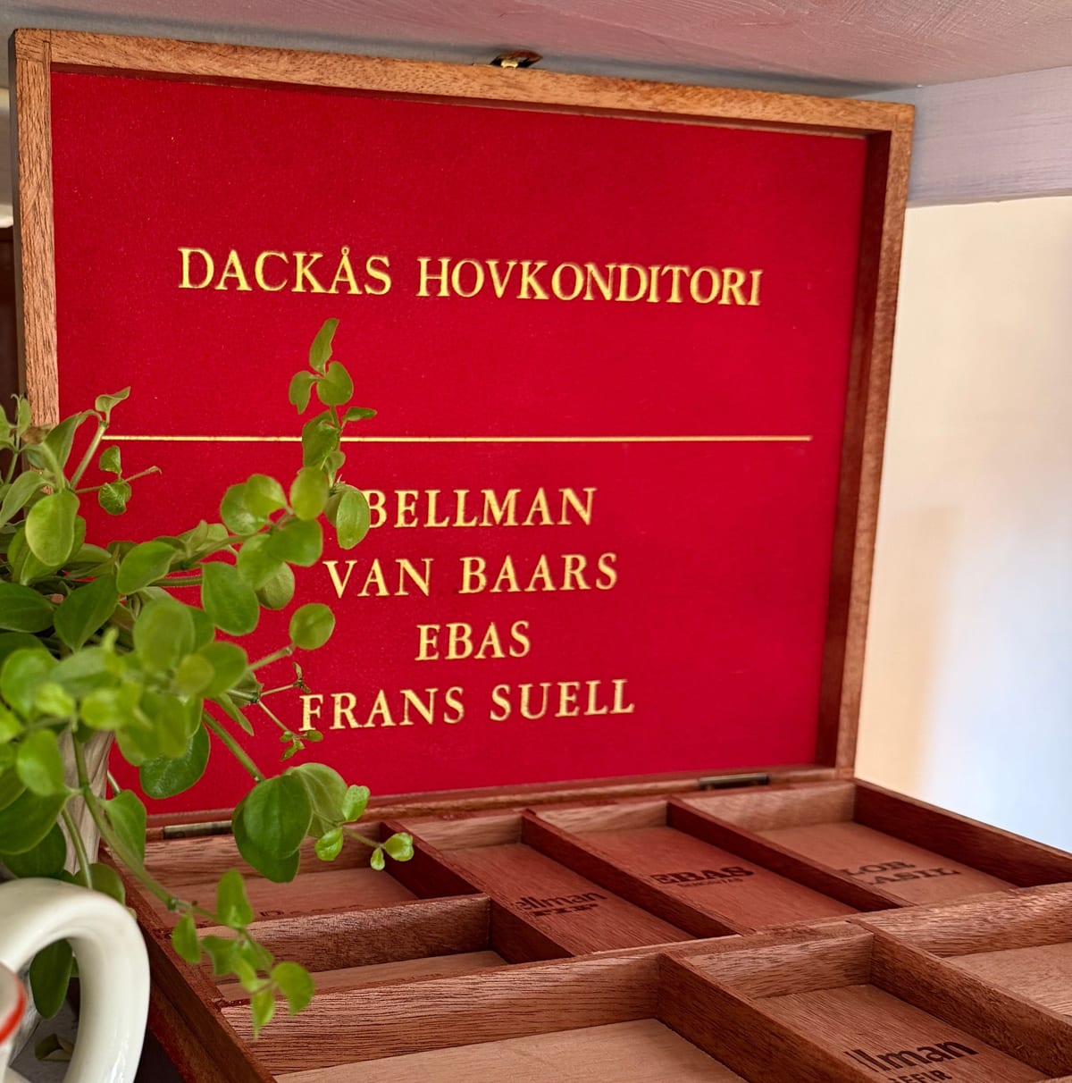 Cigarrlåda i trä med röd sammetsinsida och guldtexten Dackås Hovkonditori – Bellman, Van Baars, EBAS, Frans Suell